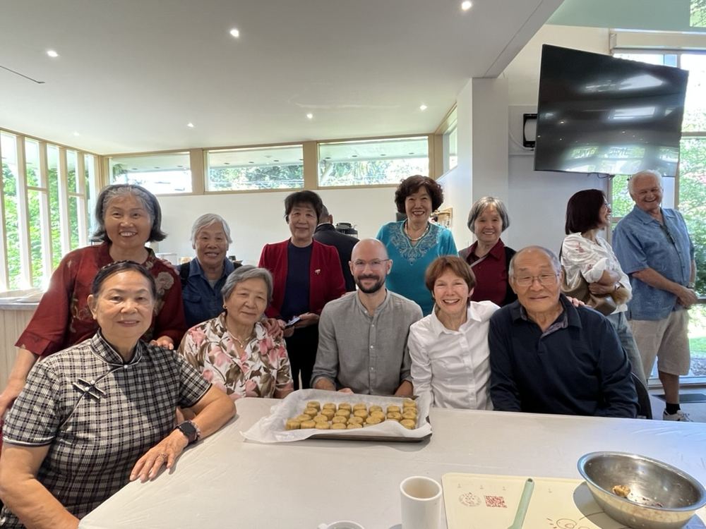 Members of the Chinese community group smiling around a table with a tray of baking they made together