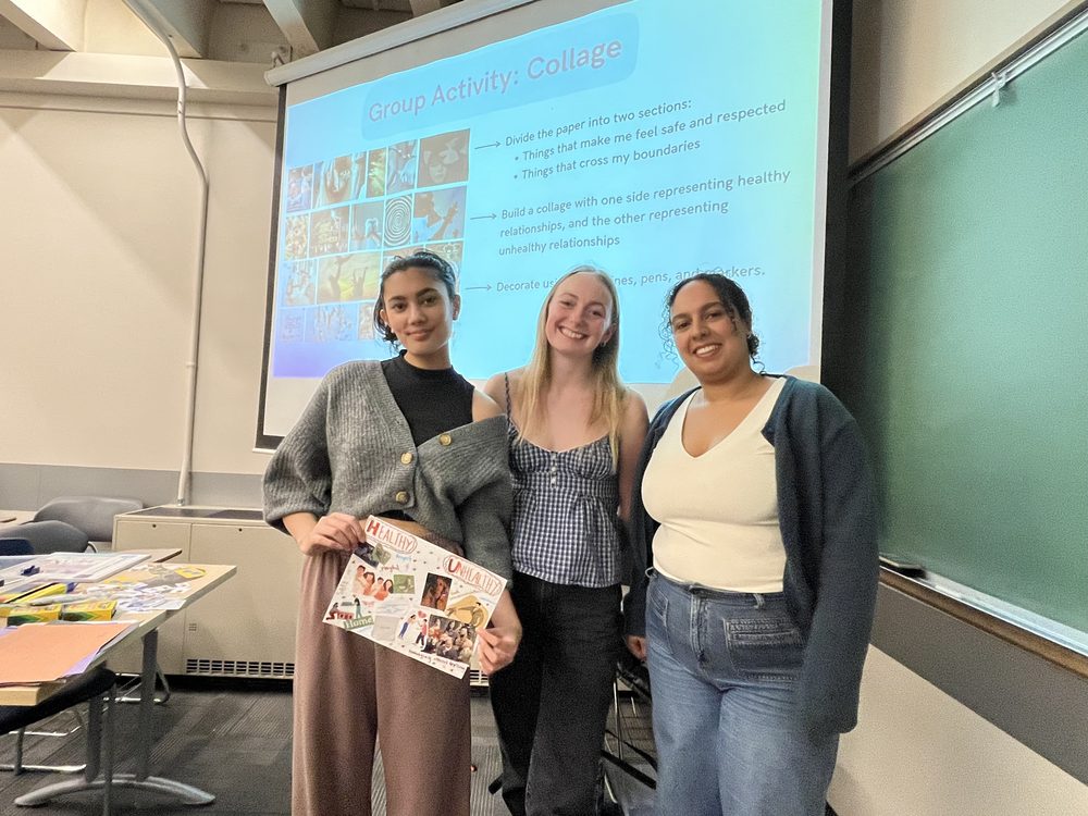 Three Youth Health and Cultural Ambassadors smiling in a classroom after a workshop, one holding a collage