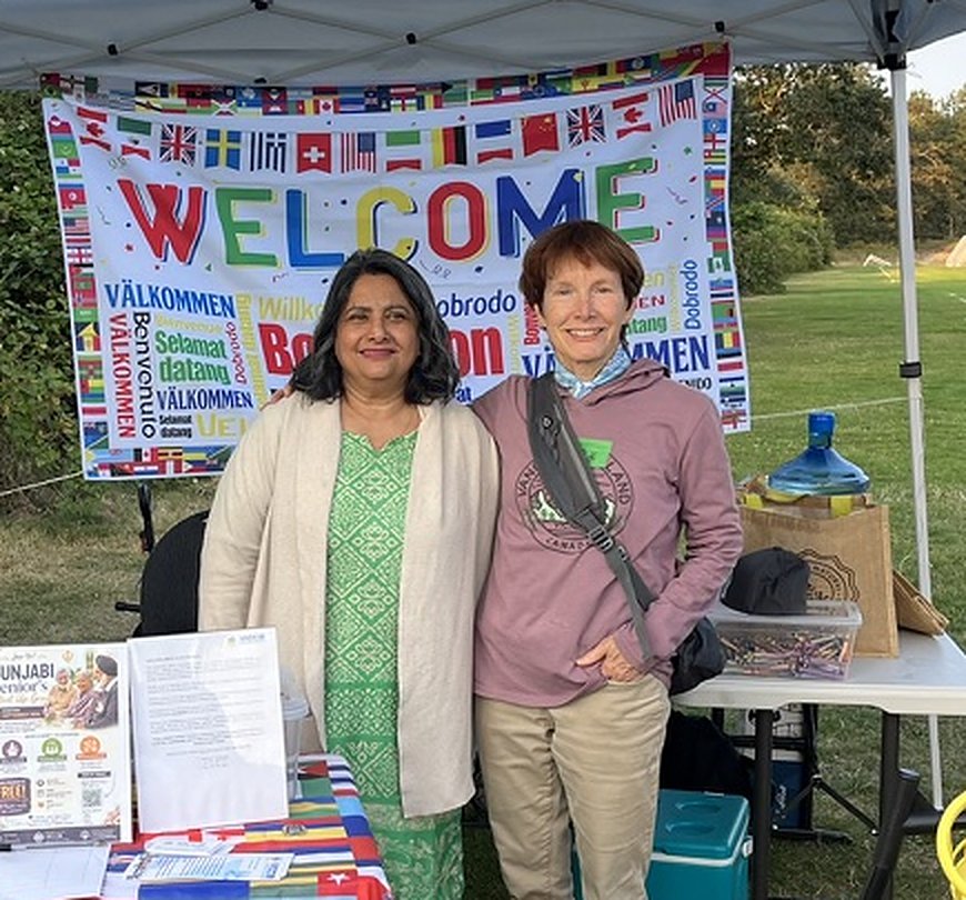 Two VICCIR team members at an outreach table under a multilingual Welcome banner
